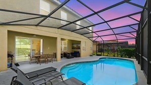A covered outdoor swimming pool with lounge chairs, a table, and a patio area. - Upstay Disney Getaway With Pool Game Room (Davenport)