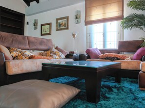 Una sala de estar con un sofá marrón, una mesa de centro de vidrio y un tapete azul.