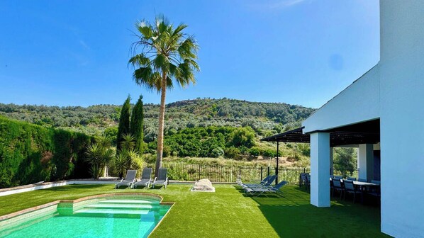 Una piscina con sillas de descanso, una palmera y vistas a un paisaje montañoso.