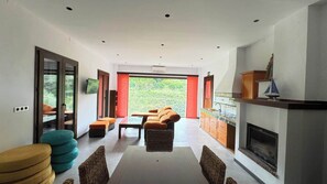 A modern interior with a dining area, sofa, fireplace, and large windows.