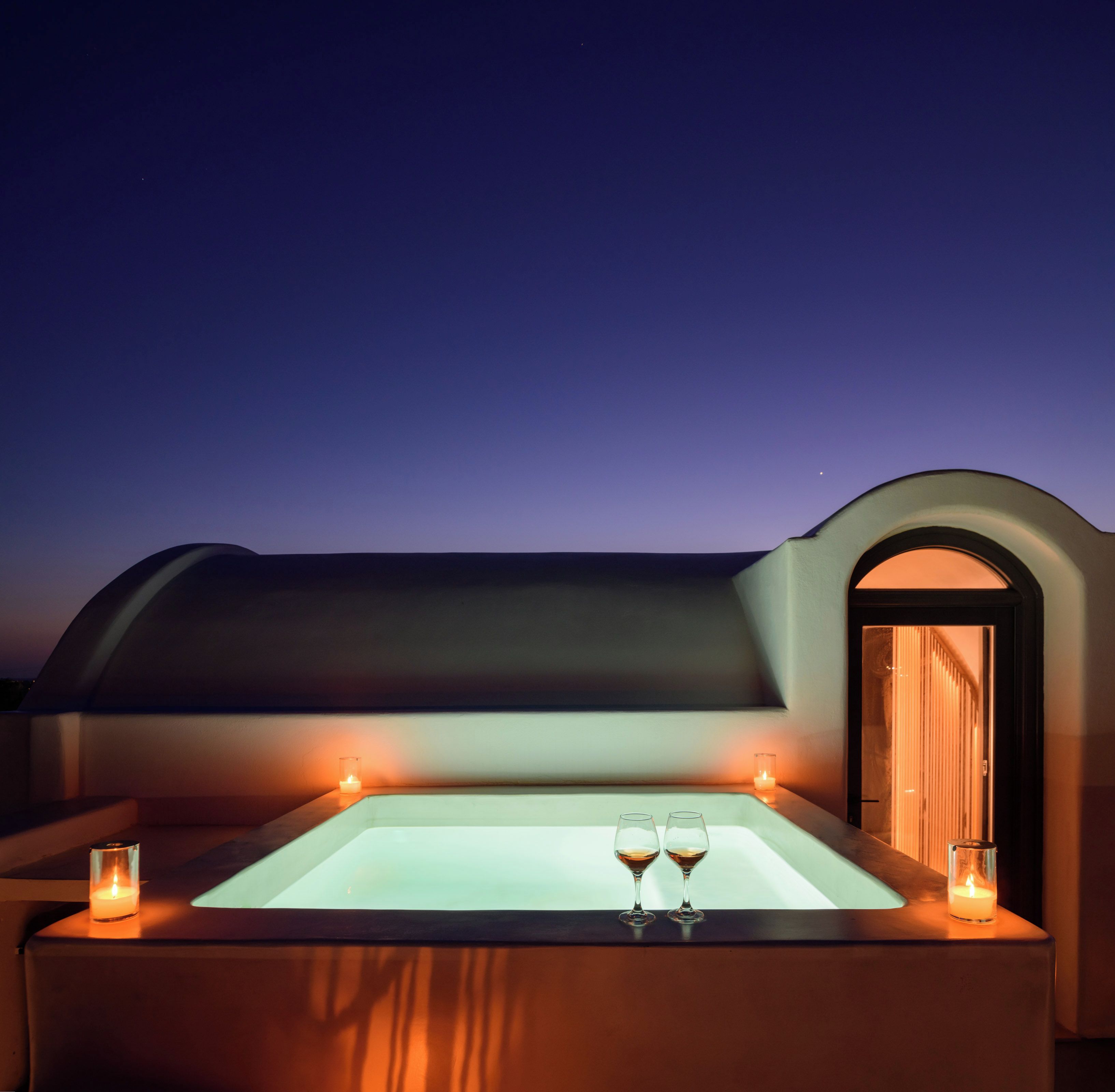 Un jacuzzi con dos copas de vino, una vela y una vista del cielo al anochecer.