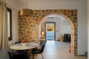 A dining area with a stone archway, a round table with chairs, and a view through an open door. - Penny's House New Luxe Jacuzzi Villa 400m from Sea (Santorini)