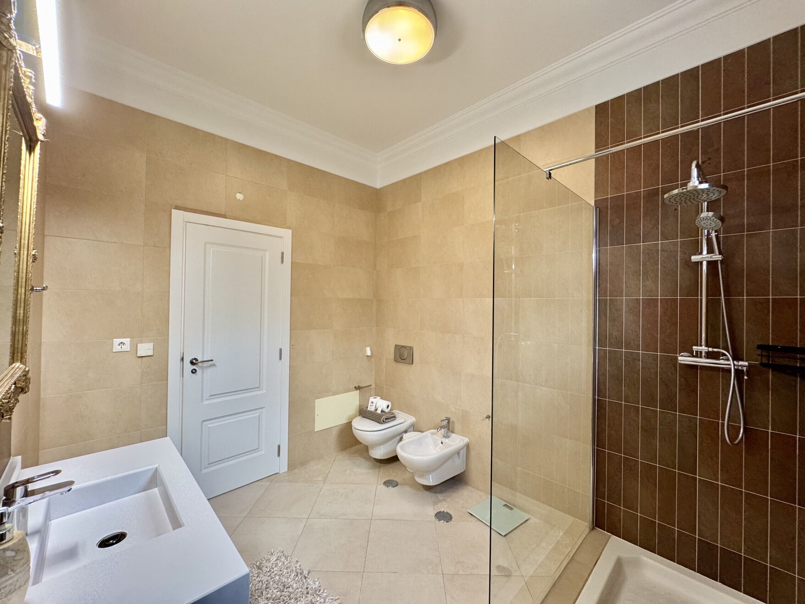 Ein Badezimmer mit einem weißen Waschbecken, zwei Toiletten, einer Dusche und einer Tür.