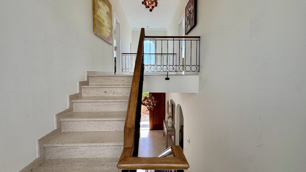 Een trap met een houten leuning die leidt naar een balkon met een metalen hekwerk.