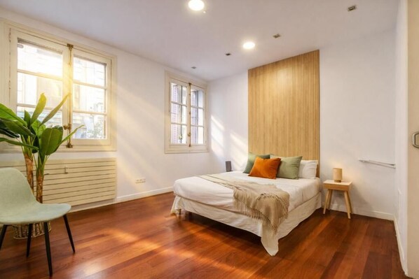 A bedroom with a bed, a chair, a small table, and a potted plant. - Collection Fuencarral (Madrid)