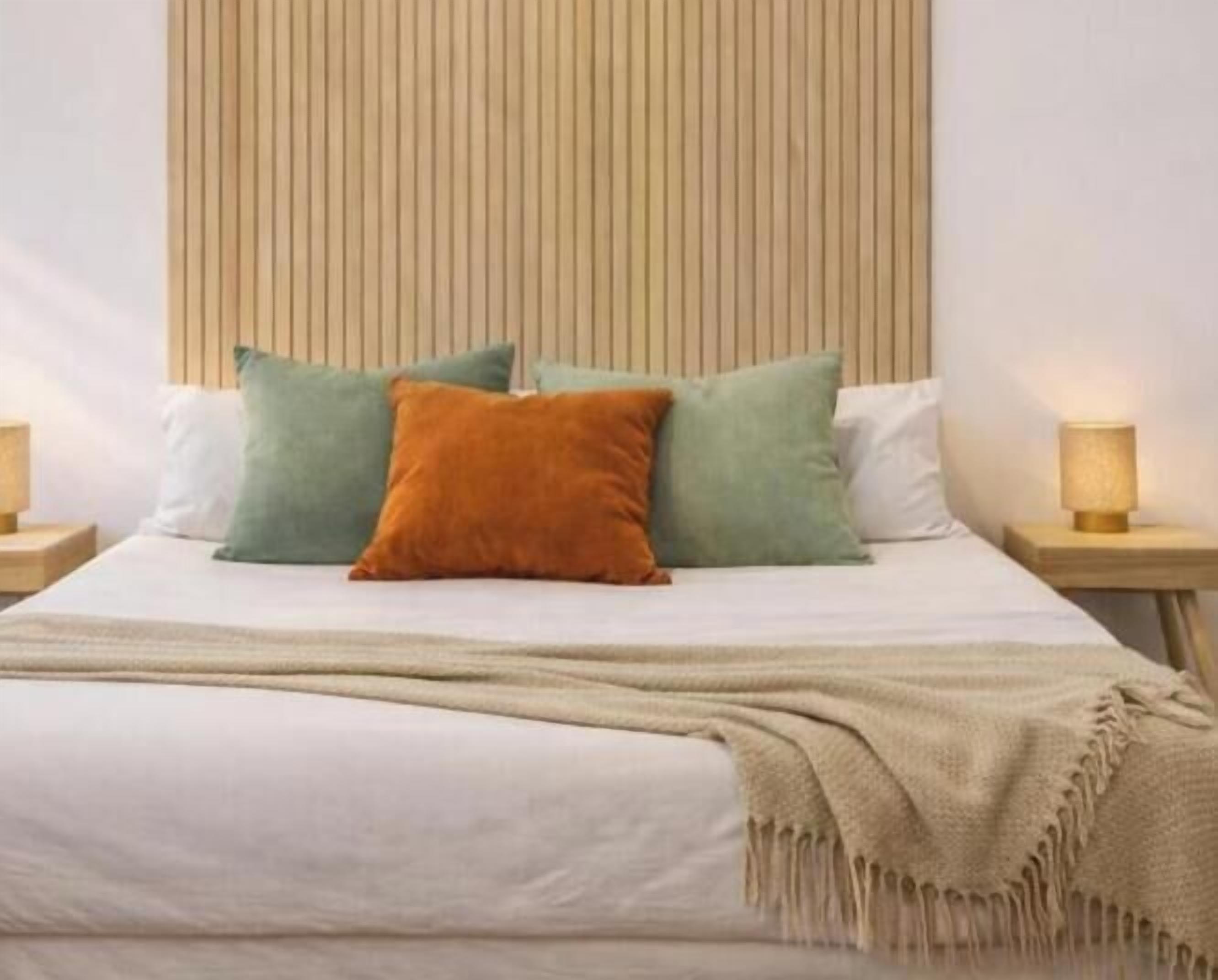 Una cama con cabecera de madera, varios almohadones y lámparas de noche.