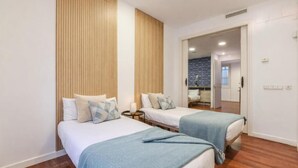 Quarto de hotel com duas camas, lambris de madeira, parede de destaque em pedra e vista para o banheiro.
