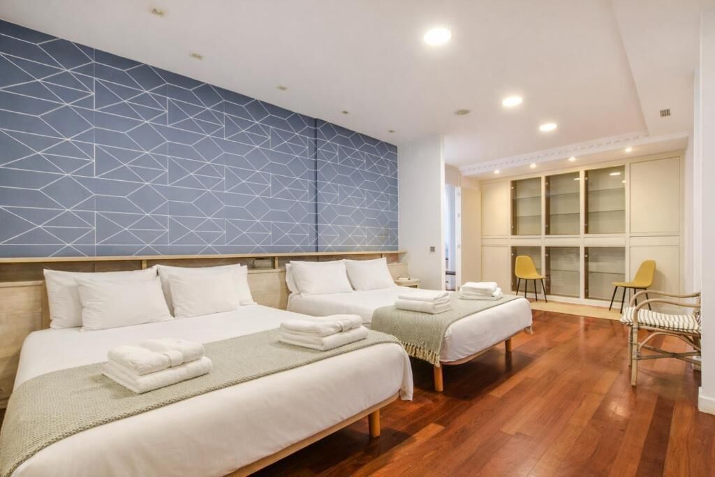 Habitación de hotel con dos camas, un muro de diseño geométrico, suelo de madera y un ventanal grande.
