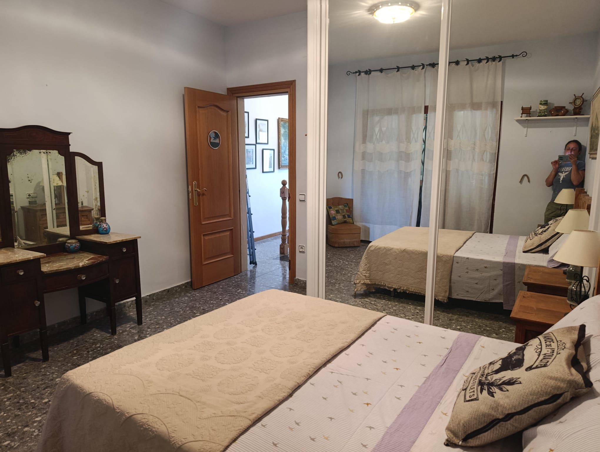A bedroom with a bed, a dresser, a mirror, and a door leading to another room.