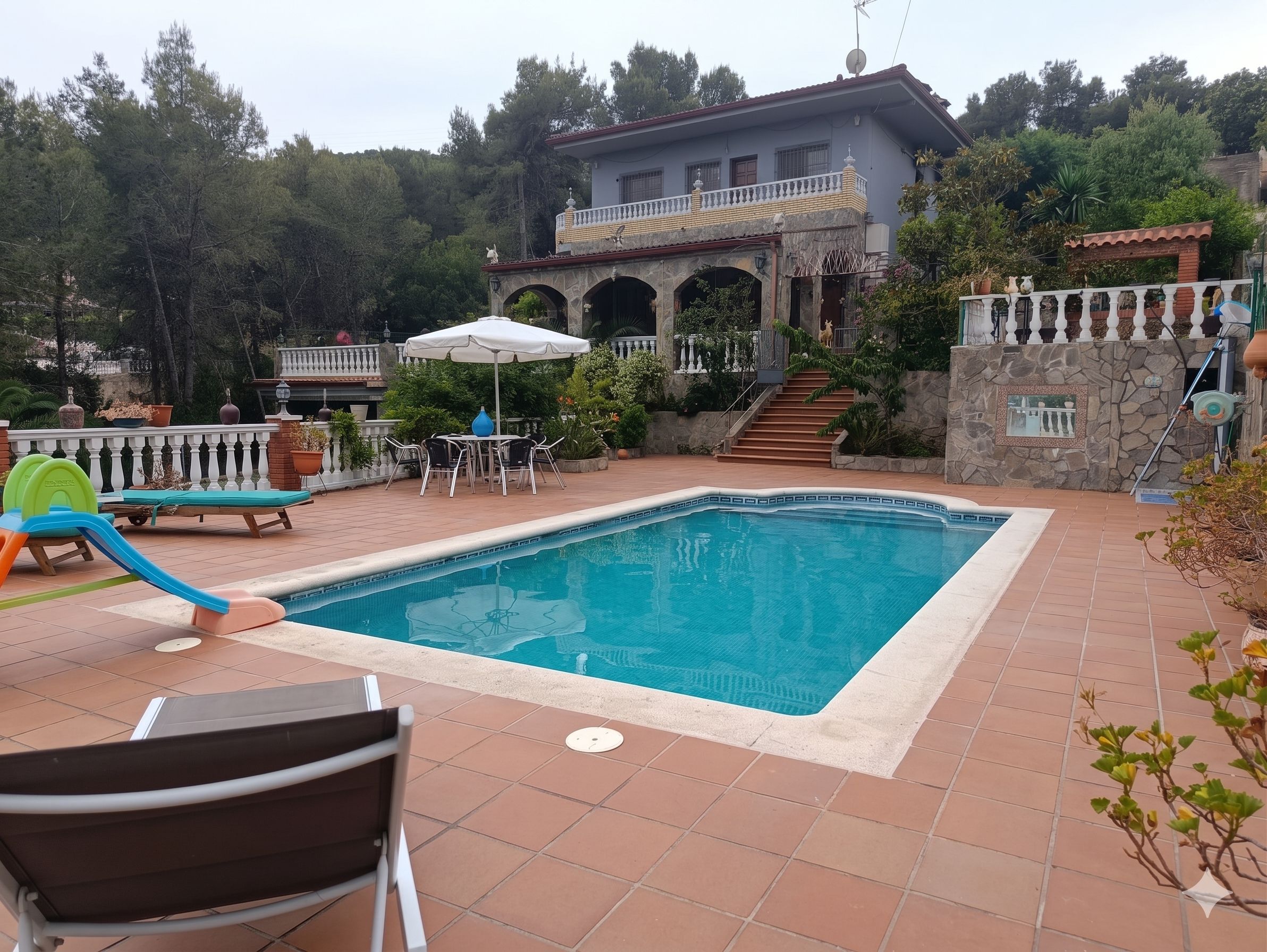 A swimming pool with a patio area, a children's play structure, and a house with a balcony.