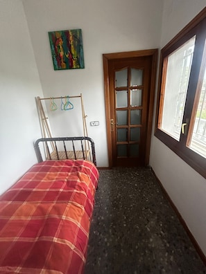 A small room with a bed, a door, a window, and a wall-mounted artwork.