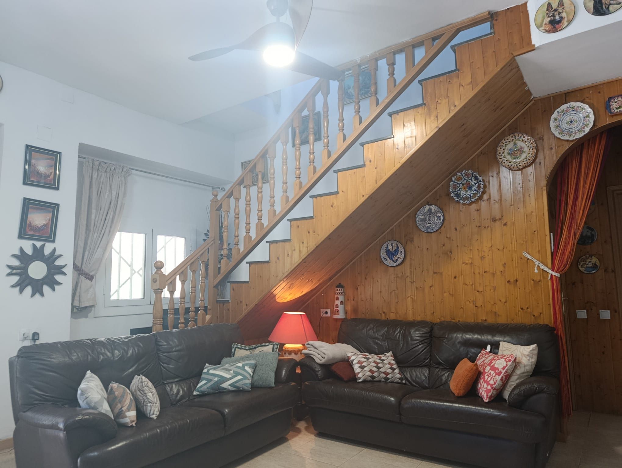 A living room with a wooden staircase, a black leather sofa, and decorative plates on the wall.