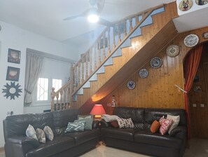 A living room with a wooden staircase, a black leather sofa, and decorative plates on the wall.