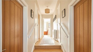 Una escalera de madera conduce a una habitación con una puerta blanca, un pequeño tapete y cuadros en las paredes.