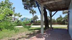 A covered patio area with a brick floor, wooden beams, and a view of a residential area with houses and palm trees. - Budget Friendly Apartment with Ample Boat Parking! (Cedar Key)