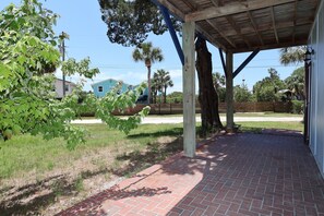 A covered patio area with a brick floor, wooden beams, and a view of a residential area with houses and palm trees. - Budget Friendly Apartment with Ample Boat Parking! (Cedar Key)