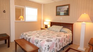 A bedroom with a bed, bedside lamps, a nightstand, a wooden bench, a mirror, and a framed picture on the wall. - Budget Friendly Apartment with Ample Boat Parking! (Cedar Key)