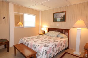 A bedroom with a bed, bedside lamps, a nightstand, a wooden bench, a mirror, and a framed picture on the wall. - Budget Friendly Apartment with Ample Boat Parking! (Cedar Key)