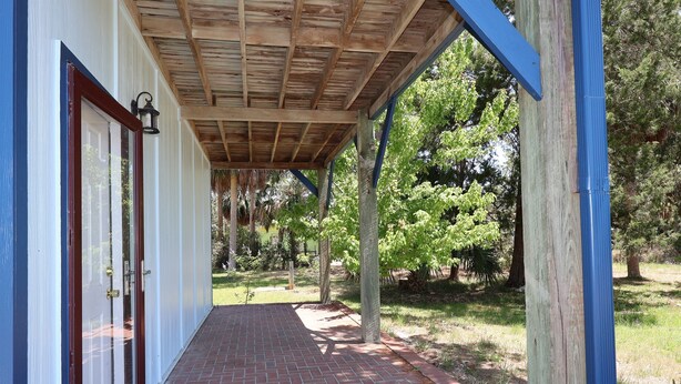 A covered porch with a brick pathway leading to a white door. - Budget Friendly Apartment with Ample Boat Parking! (Cedar Key)