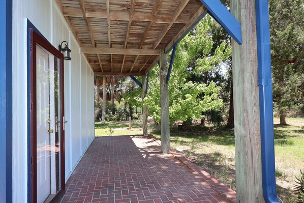 A covered porch with a brick pathway leading to a white door. - Budget Friendly Apartment with Ample Boat Parking! (Cedar Key)