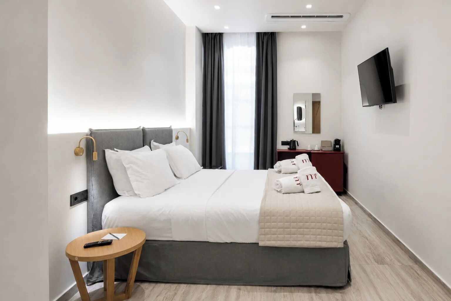 A modern hotel room with a bed, bedside table, TV, and a mirror.