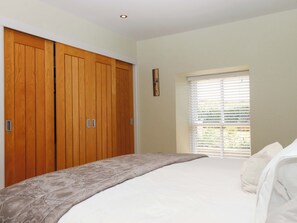 A bedroom with a large bed, wooden wardrobe, and a window with blinds. - Duke's Barn (Totnes)