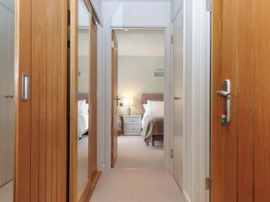 A hallway leading to a bedroom with a bed, bedside table, and lamp. - Duke's Barn (Totnes)