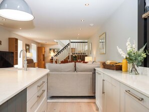 A modern kitchen with a built-in oven, a dining area with a table and chairs, and a staircase leading to an upper level. - Duke's Barn (Totnes)