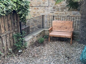 A wooden bench against a stone wall, surrounded by gravel and a metal fence. - 2 West View (Richmond)