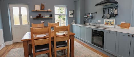 Une cuisine avec des chaises en bois, un lustre, une cuisinière et une fenêtre.