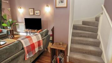 A living room with a sofa, a TV, a bookshelf, and a staircase.