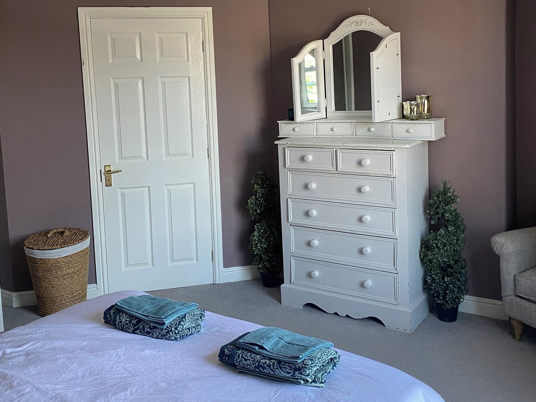 A bedroom with a white bed, a white dresser with drawers, a mirror, and a door.