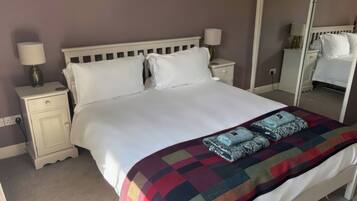 Una cama bien hecha con una manta y almohadas coloridas, una mesita de noche con una lámpara y un espejo en la pared.