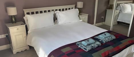 A neatly made bed with a colorful blanket and pillows, a bedside table with a lamp, and a mirror on the wall.