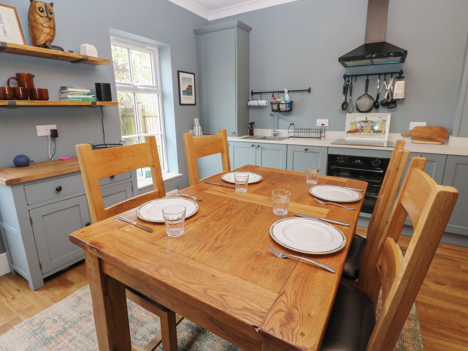 Une cuisine avec une table en bois dressée pour quatre personnes, des chaises, une cuisinière et divers ustensiles de cuisine.