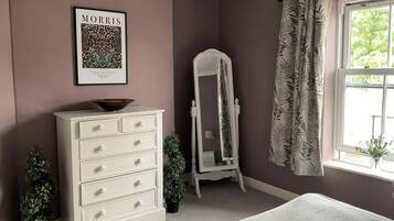 A bedroom with a dresser, a mirror, a bed, a window with curtains, and a framed picture on the wall.