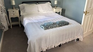 Ein ordentlich gemachtes Bett mit gemustertem Überwurf und zwei Kissen, flankiert von Nachttischen mit Lampen, in einem Zimmer mit hellblauer Wand und einem gerahmten Kunstwerk darüber.