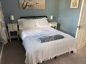 A neatly made bed with a patterned bedspread and two pillows, flanked by nightstands with lamps, in a room with a light blue wall and a framed artwork above the bed. - 2 West View (Richmond)