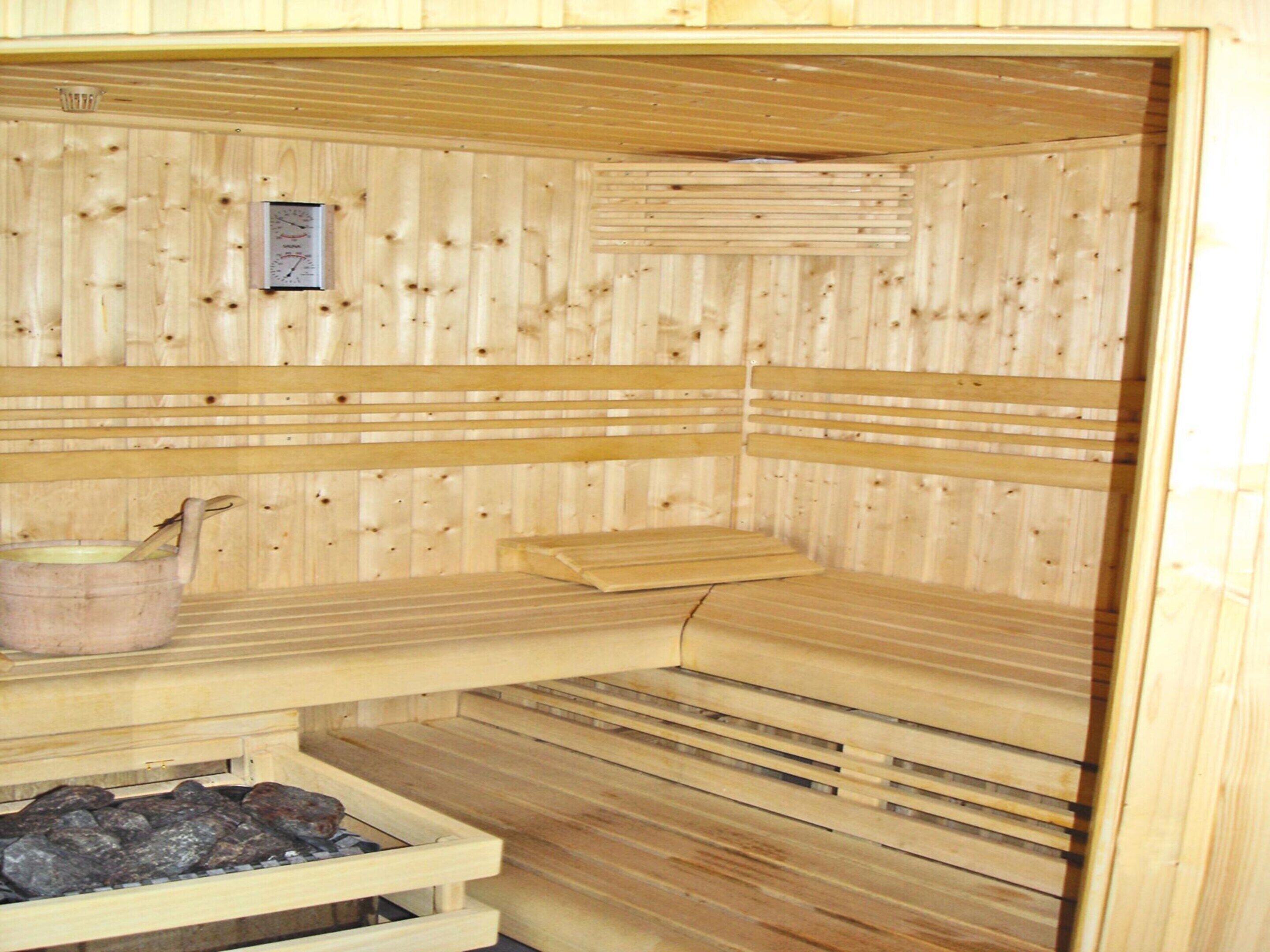 A sauna with wooden benches, a bench with a towel, and a bucket with a ladle.
