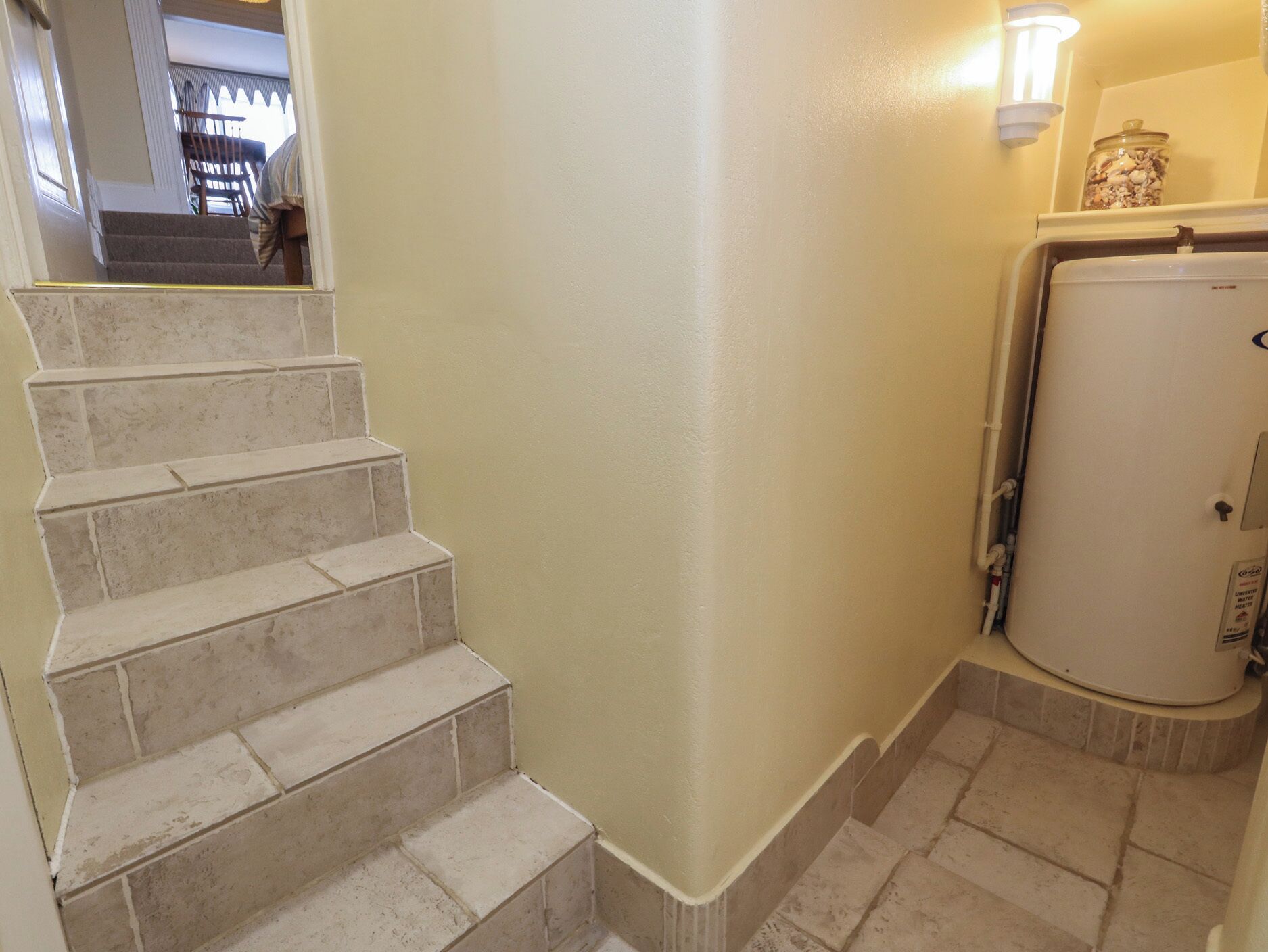 A staircase with beige tiles leading to a landing, a white wall, and a white appliance in the corner.