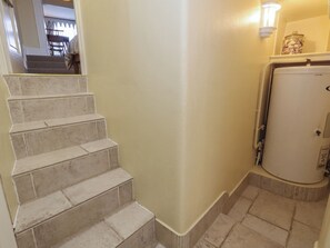 Eine Treppe mit beigefarbenen Fliesen führt zu einer Zwischenebene, an einer Wand ist Weiß zu sehen und in der Ecke steht ein weißes Gerät.