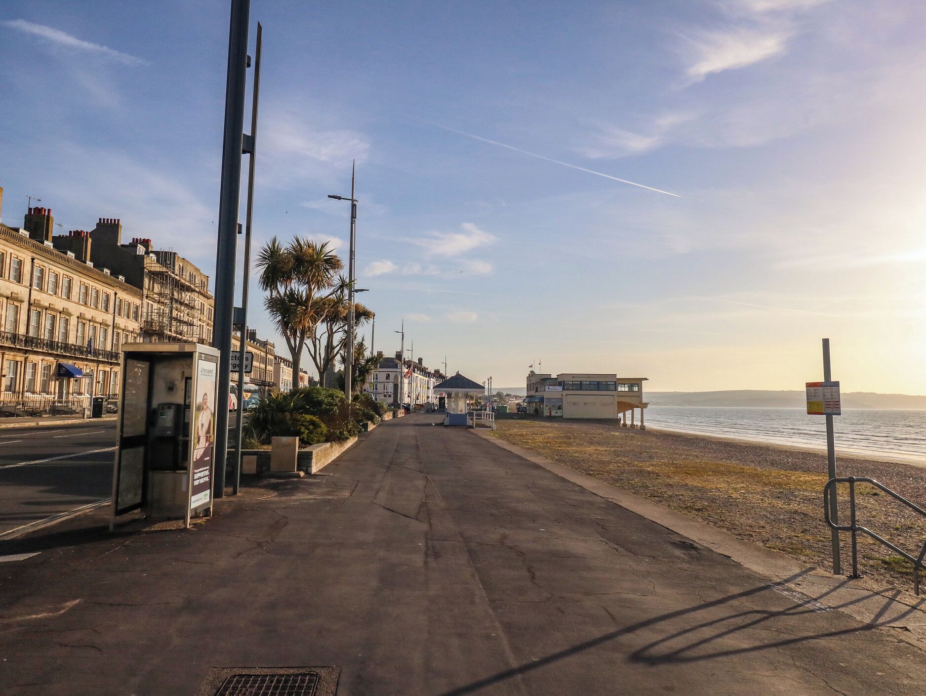 A coastal road with a bus stop, a beach, and buildings along the shore.
