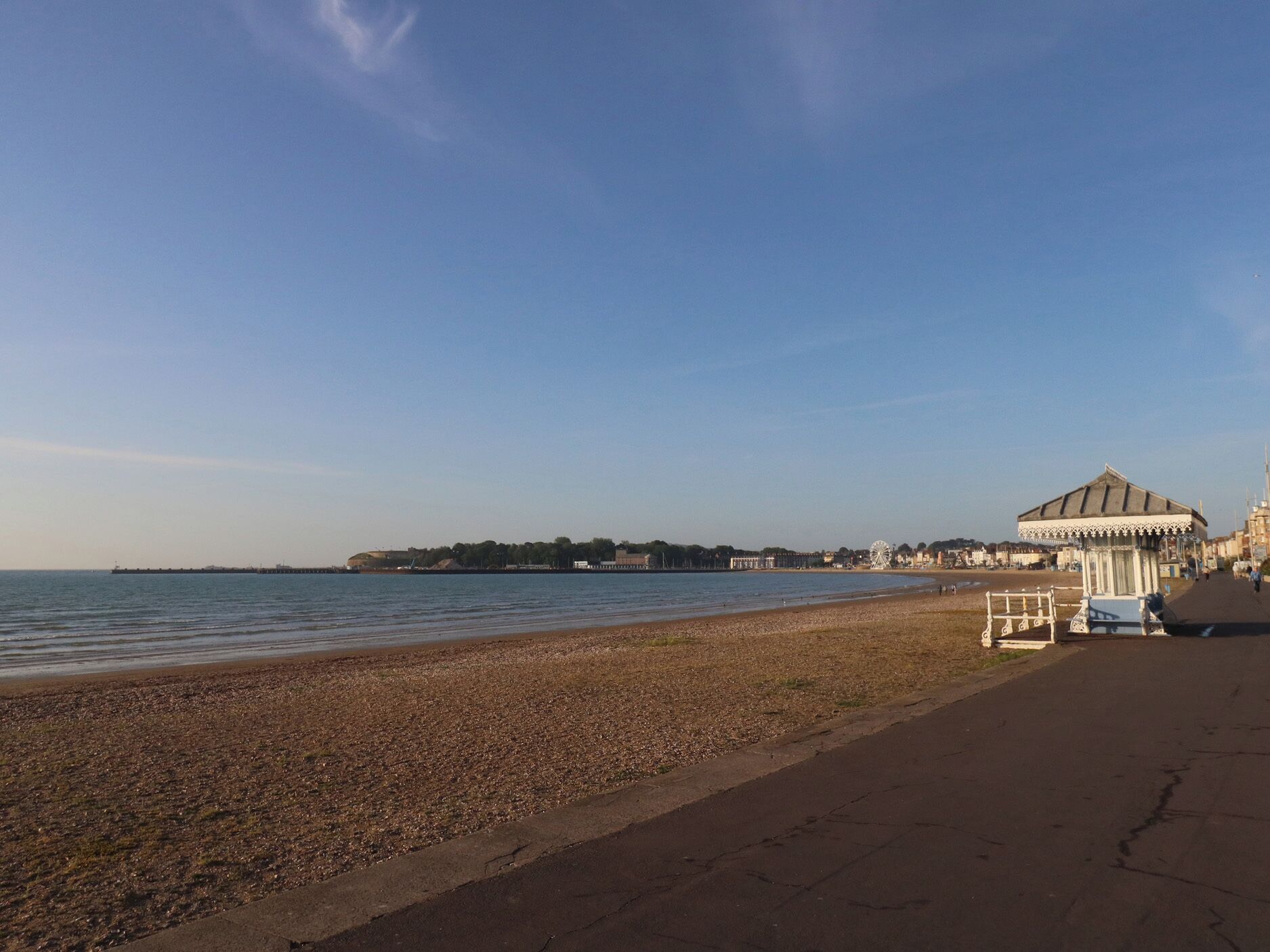 A beach with a pier, a white gazebo, and a Ferris wheel in the background.