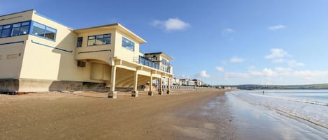 A beachfront building with multiple balconies, a sandy beach, and a clear sky.