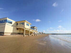 Ein Gebäude direkt am Strand mit mehreren Balkonen, einem Sandstrand und blauem Himmel.