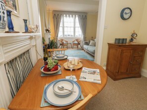 A dining area with a table set for two, a fireplace, a clock on the wall, and a view into the living room. - Number 3 by the Sea (Weymouth)