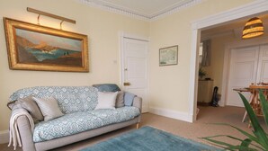 A living room with a sofa, a rug, a painting, and a door. - Number 3 by the Sea (Weymouth)