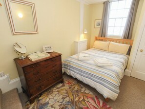 A bedroom with a bed, a dresser, a mirror, a bedside lamp, and a window with curtains. - Number 3 by the Sea (Weymouth)