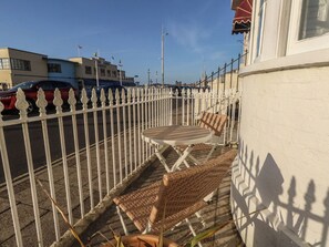 Un balcon agrémenté de meubles en osier, une clôture blanche et un bâtiment sur lequel on peut voir une enseigne.