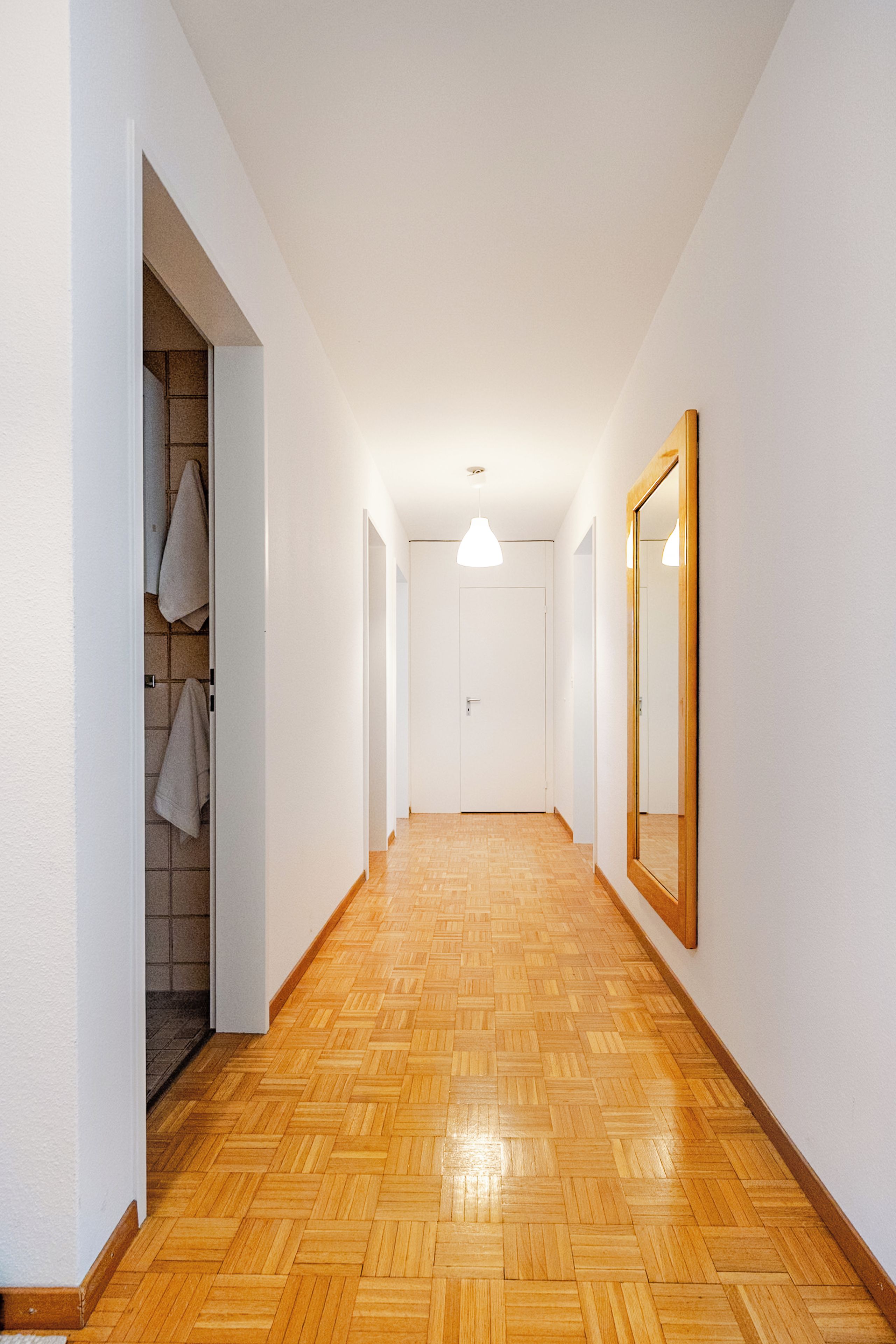 A hallway with wooden flooring, white walls, and a door at the end.